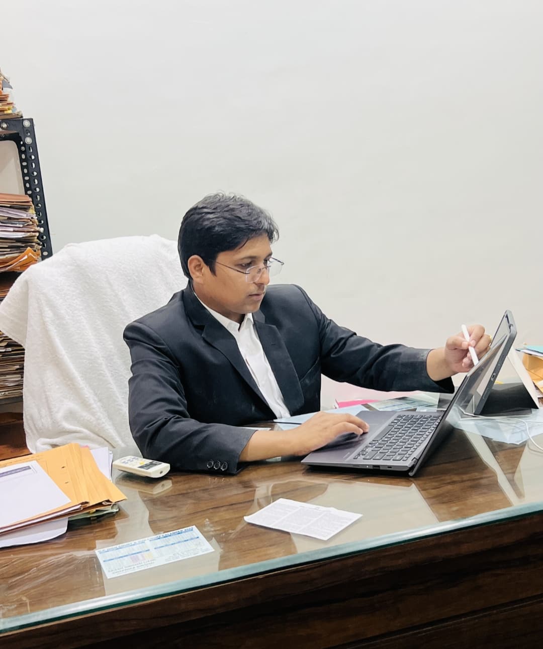 Man in a suit using a laptop and tablet with a stylus at his desk.